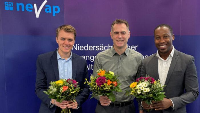 Justin Hoop, Sven Thren und Kelvin Enwemeka stehen vor der NEVAP-Wand